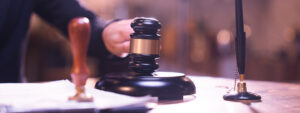 A gavel resting on a wooden block with a pen on a desk, indicating a legal setting.